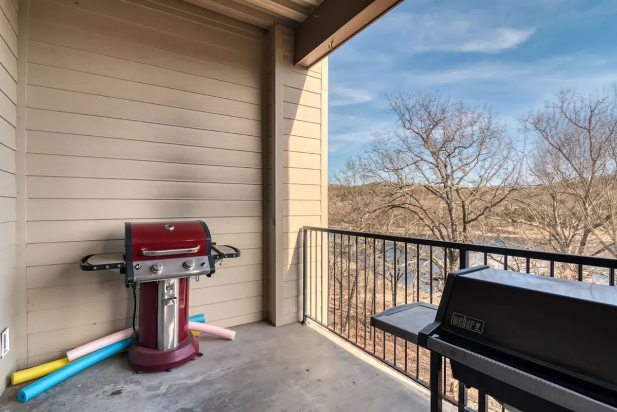 An exterior deck area with a red gas grill, black grill, and balcony view overlooking the lake. The setup invites guests to enjoy outdoor dining, barbecuing, and taking in tranquil lakefront scenery.
