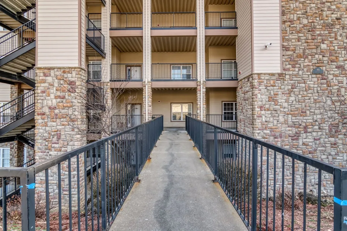 This image captures the walkway leading to the entrance of the building, featuring stone-clad pillars and balconies with railings. The scene suggests accessibility to outdoor spaces and encourages social gatherings on the balconies, evoking a sense of arrival and an invitation to explore the surroundings.