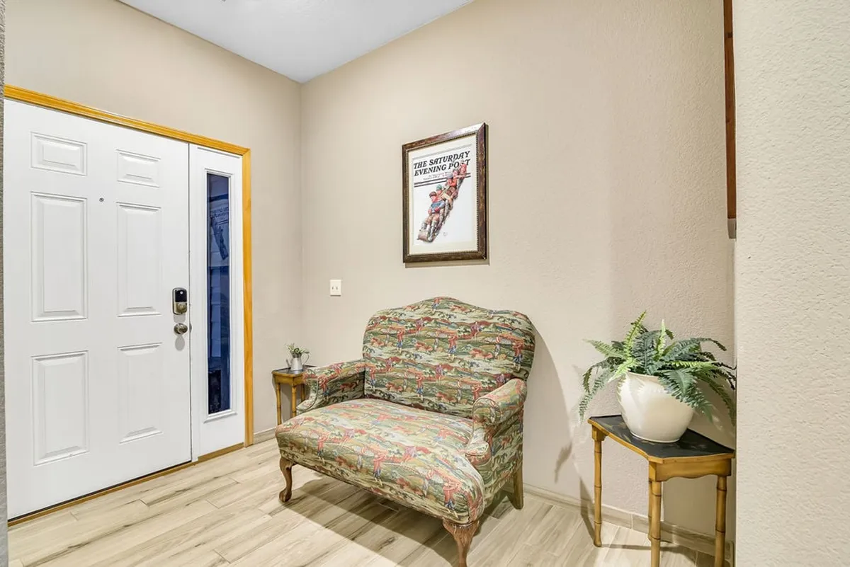 A cozy interior entryway featuring a decorative armchair, framed artwork, a side table with a plant, and the main entrance door. The scene is inviting and warm, suggesting a comfortable return after a day of exploration.