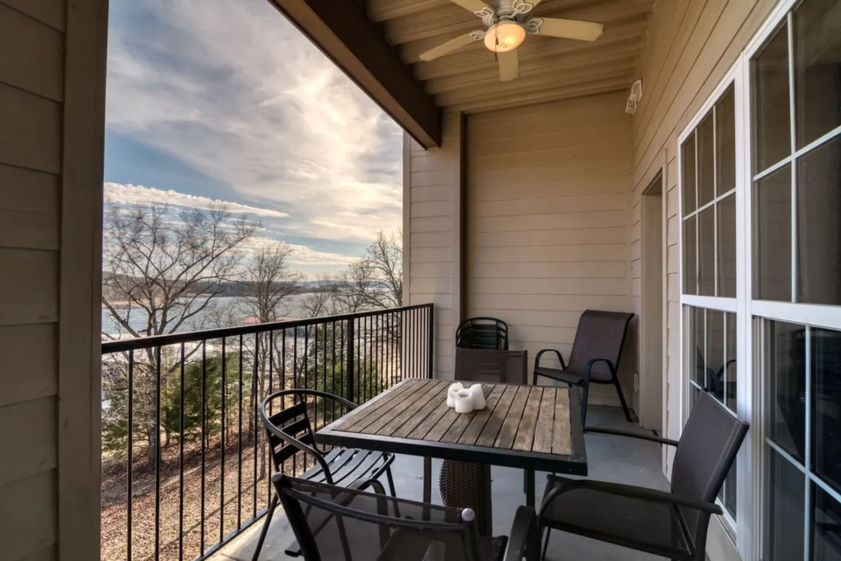 A stylish outdoor table set with decorative items and comfortable chairs overlooks a serene lake. The space is ideal for relaxing or socializing, with an inviting sun deck atmosphere and expansive water views.