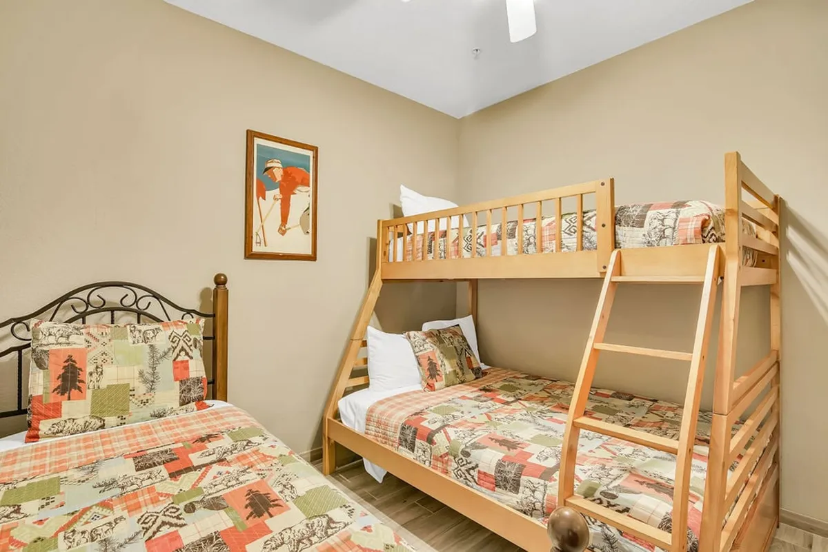 A playful bunk room with a twin-over-full bunk bed, colorful quilted bedding, and a touch of vintage artwork. The cheerful decor and layout evoke fun and togetherness, perfect for kids.