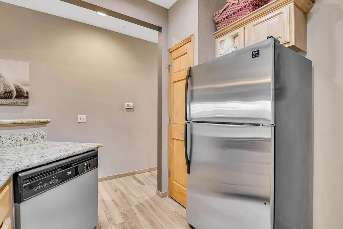 A modern kitchen scene with a stainless steel refrigerator, granite countertops, and a dishwasher, highlighting a functional cooking and meal prep area designed for sharing meals and culinary experiences.