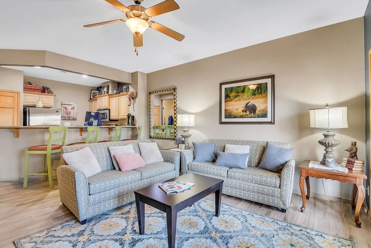 A welcoming view of the open-concept living area, featuring cozy sofas, a coffee table, a kitchen bar, and tasteful artwork and lighting. The arrangement emphasizes a seamless flow between spaces for relaxation, socializing, and informal dining.
