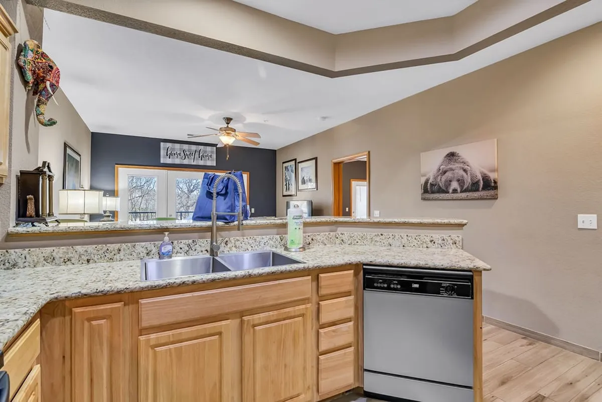 A spacious, open-concept kitchen featuring a large granite island with double sinks, surrounded by plenty of seating for gathering. The area is set up to accommodate group cooking and entertaining, with inviting lighting and welcoming decor that encourages family interaction and shared meals.