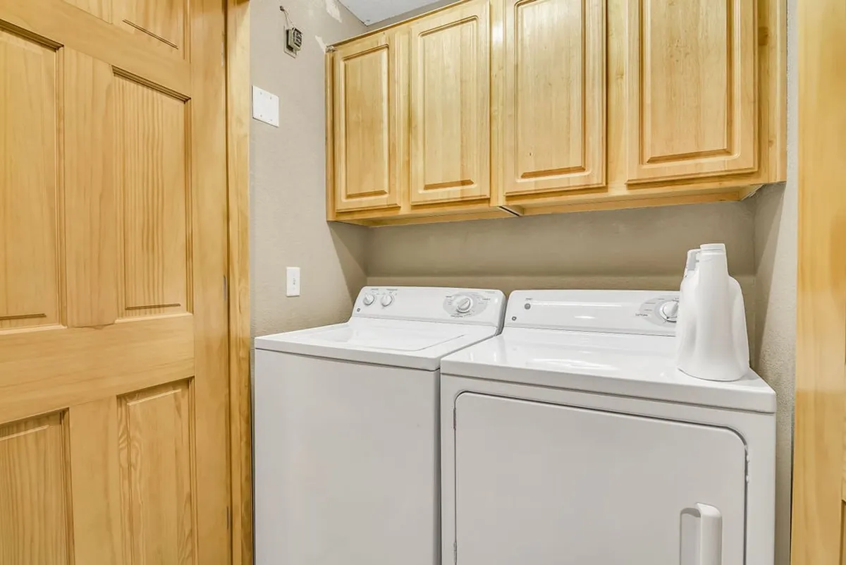 A tidy laundry room with a modern washer and dryer set, wooden cabinets above for storage, and an organized, clutter-free feel. The space exudes efficiency and orderliness.